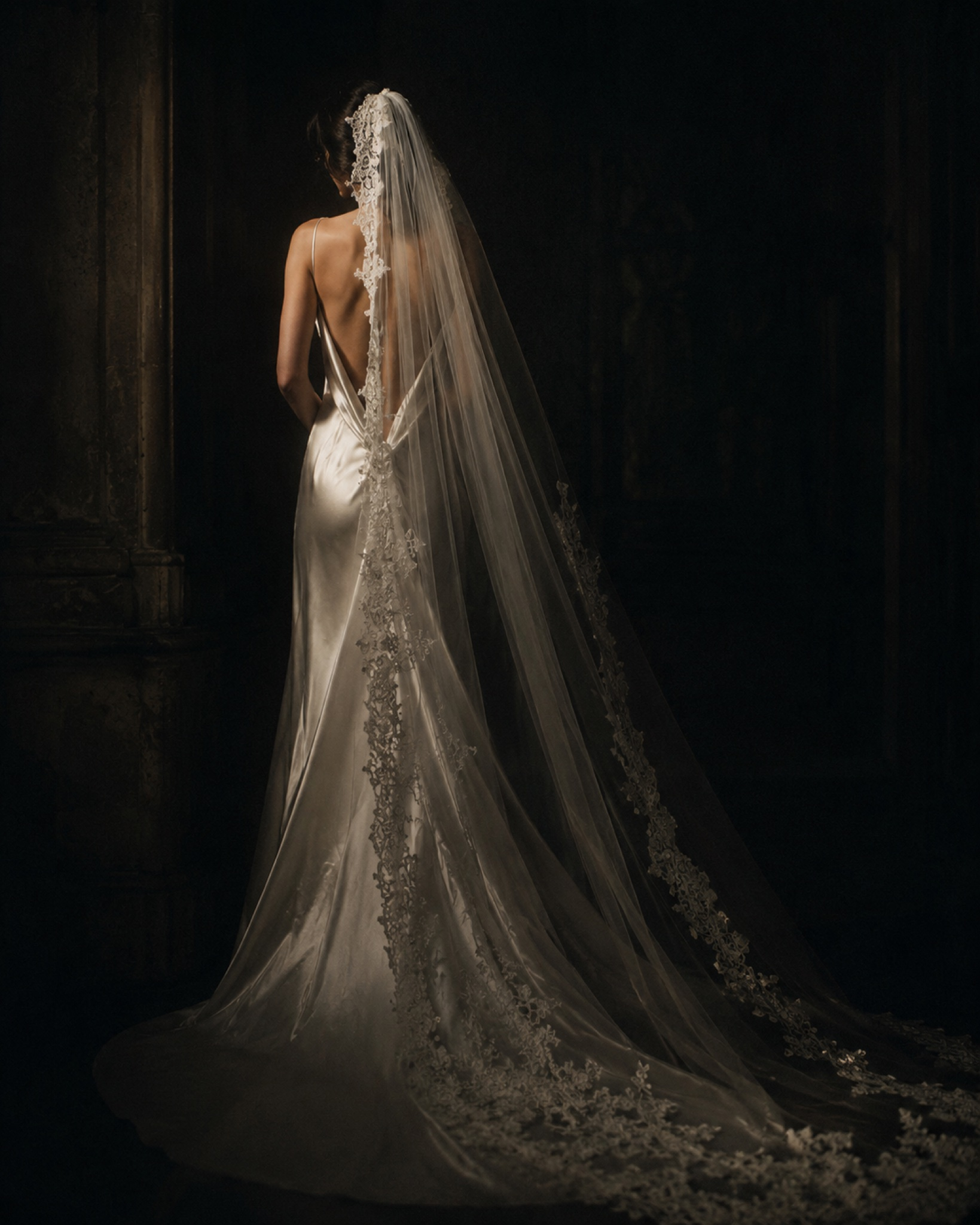 Bride from behind in a lace-trimmed veil and satin gown