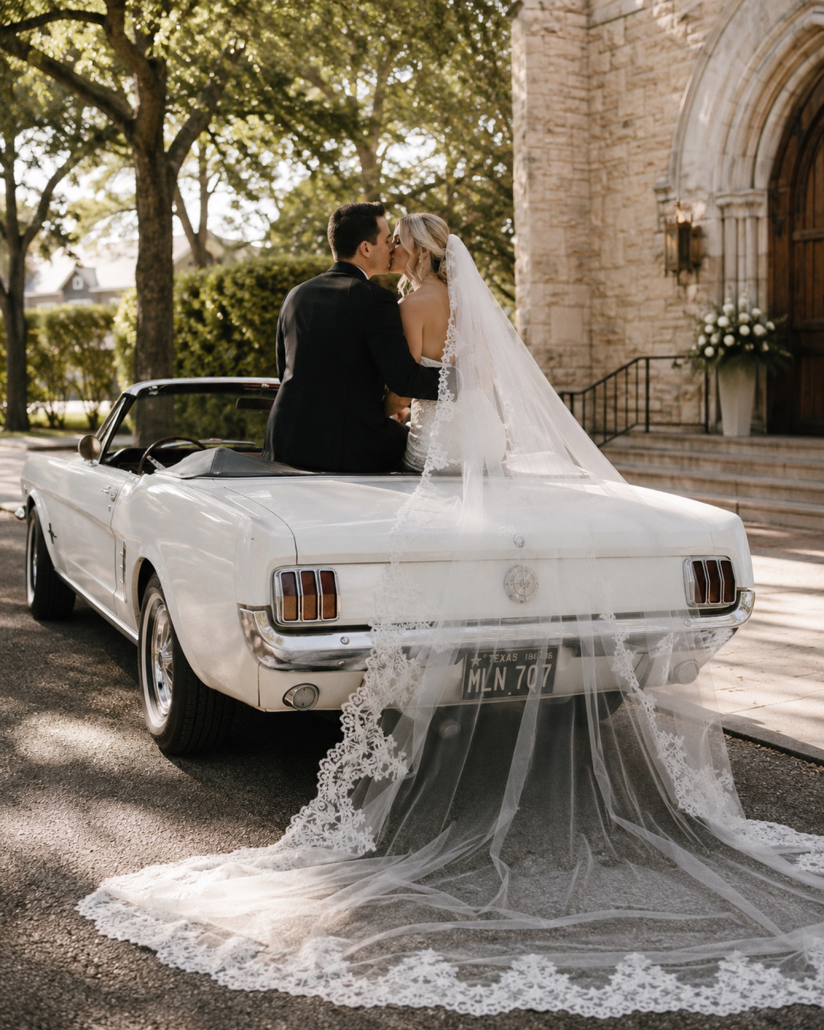 Bride and groom kissing beside a vintage convertible outside a venue